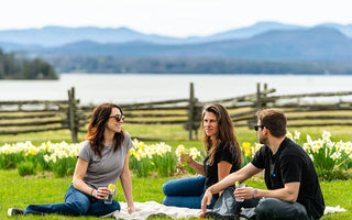 man and two women in 4T2D brand clothing sitting on blanket with Vermont Lake Champlain and Adirondack Mountains in background